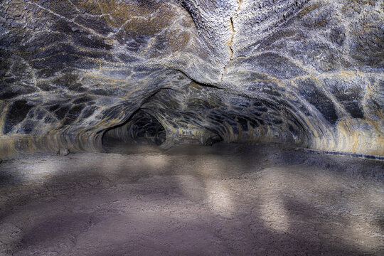 View inside a dark basalt lava tube cave with textured walls and a smooth floor at Lava Beds National Monument in California.