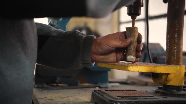 Close-up of a knife maker's hands drilling holes into knife handles using a power machine in his workshop. Concept of knife making, craftsmanship, precision manufacturing, metalworking, artisanal prod
