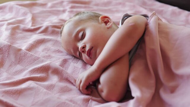 Cute little toddler boy sleeping peacefully under soft pink blanket in cozy bed at home resting during quiet daytime nap