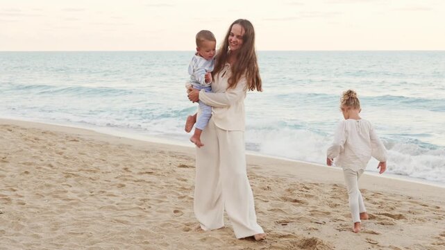 Loving mother holding her small toddler son on arms while playing with her little daughter on sandy sea beach