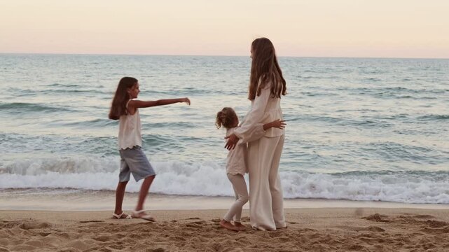 Happy family with two daughters holding hands in circle on sandy sea beach during peaceful summer evening walk