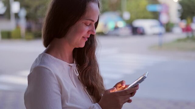 Side view profile of young woman holding smartphone and typing message outdoors on city street