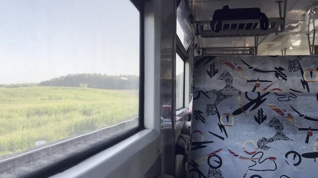 Countryside view through a train window beside an empty patterned passenger seat. Rail travel, rural landscape, public transport and journey concept