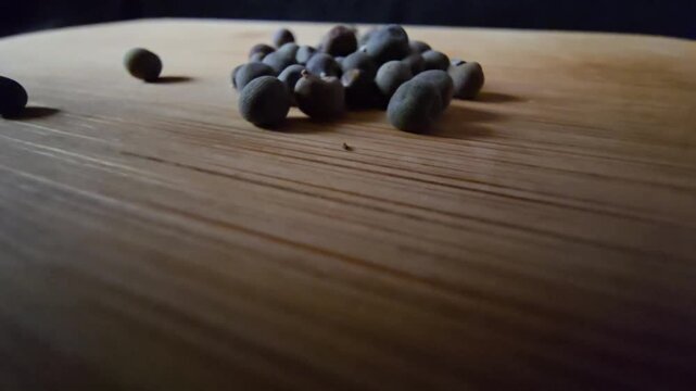 Low-angle video of grouped and scattered dry okra seeds on a wooden board, highlighting textures and earthy tones for agricultural and cooking projects.   
