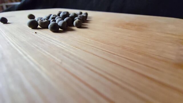 Low-angle video shot of clustered dried okra seeds on a wooden board, featuring natural textures, earthy green-brown tones, and a shallow depth of field for agricultural themes.   