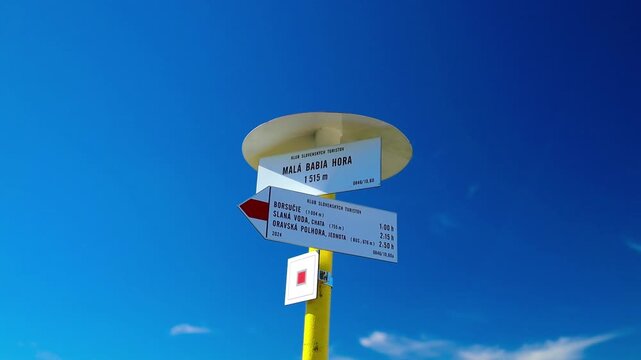 Close-up of a tourist directional wooden sign with arrows indicating hiking routes on a trail under a bright blue sky. 