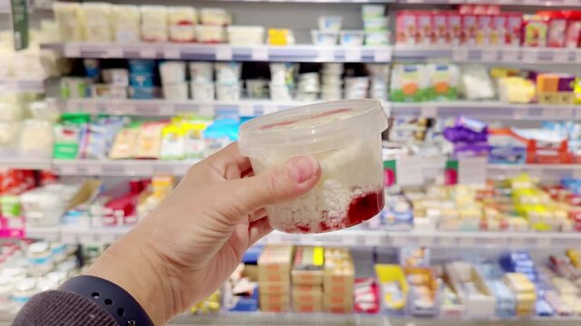 Hand Holding Cottage Cheese in Supermarket &ndash; Dairy Products in Front of Blurred Shelves