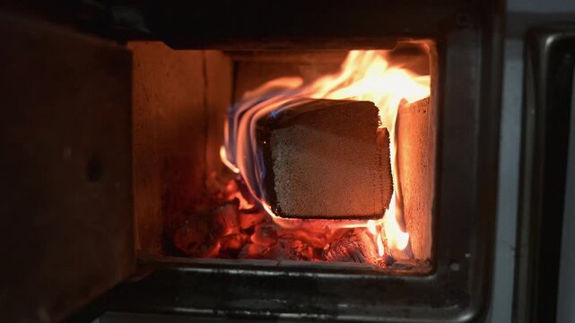 Wood-burning stove with an active fire and a burning fuel log inside. Cozy indoor heating with bright flames inside a cast iron wood stove.
