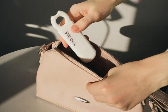 Woman's hands placing portable pill box into pink purse, managing daily medication