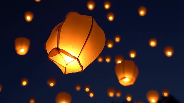 Glowing sky lantern drifting upward at night with floating bokeh lights in dark blue sky 60 FPS