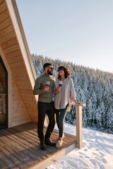 Fototapeta premium Couple enjoying wine on a snowy cabin balcony with pine forest view for winter vacation lifestyle banner and cozy holiday background