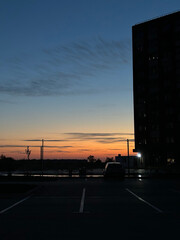 Fototapeta premium Evening sunset skyline over waterfront with silhouetted building and parked car for background and website header design