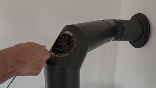 Man cleaning soot from fireplace flue pipe with flexible wire brush tool.