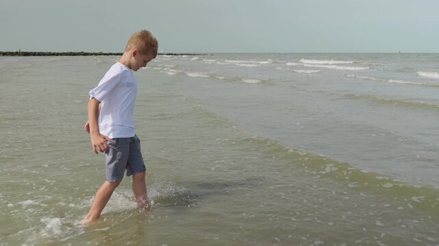 Barefoot boy walking through shallow sea water at the beach