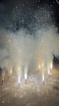 Several ground fountain fireworks erupt simultaneously on a flat surface, shooting bright sparks and thick smoke into the night air.
