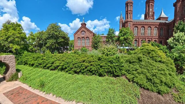 Camera tilts upward from garden groundcover toward the Smithsonian Castle facade in Washington.
