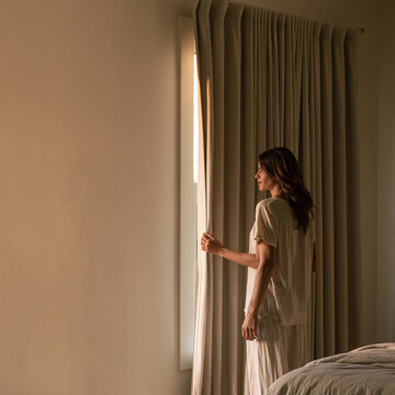 Woman drawing a bedroom curtain in soft daylight