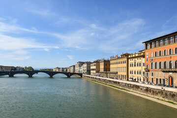 Fototapeta premium Arno river view with historic buildings and Ponte Santa Trinita bridge under blue sky in Florence, Tuscany, Italy