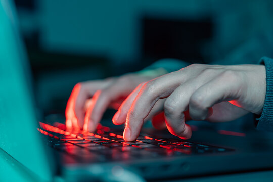 Close-up of hands typing on a glowing mechanical keyboard in the dark &ndash; Metaphor for cyber security, programming, and digital work