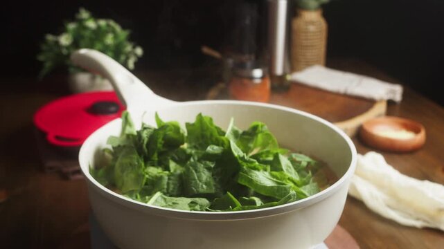 Cook adds green spinach leaves to sizzling chopped sausage and mixes everything with a spatula in a hot frying pan. Cooking process stage for quick meal prep or a creamy one-pot rice recipe.