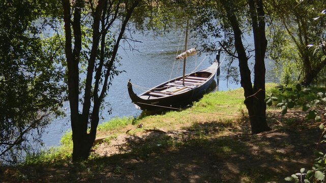 Traditional wooden river boat moored on a shady grassy riverbank