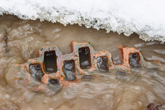 Hollow red brick partially submerged in muddy spring meltwater with white ice edge, close-up shot capturing texture and contrast of materials during seasonal thaw