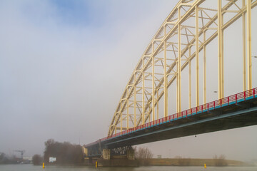 A striking steel bridge spans the foggy Noord River near Alblasserdam. Ideal for transportation, engineering, infrastructure, travel, and atmospheric landscape concepts. © TTStock Photography