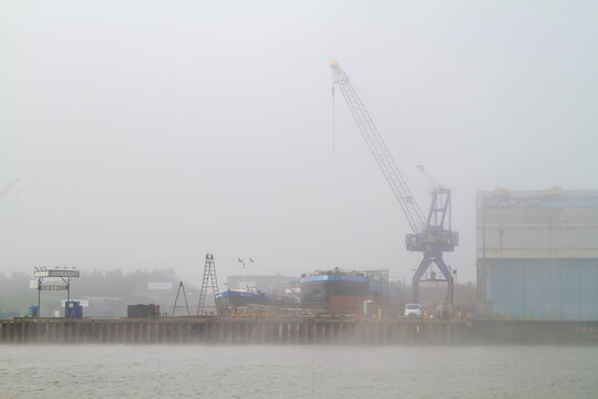 Rotterdam, Netherlands - March 11, 2015: Cargo vessels rest along the mist-covered Oude Maas near Rotterdam, framed by cranes and containers. Ideal for logistics, shipping, and industry concepts.
