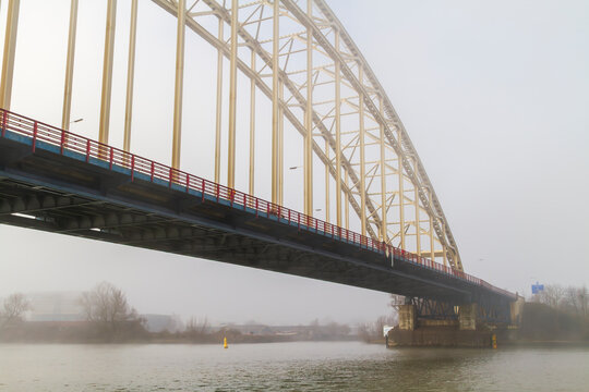 A striking steel bridge spans the foggy Noord River near Alblasserdam. Ideal for transportation, engineering, infrastructure, travel, and atmospheric landscape concepts.