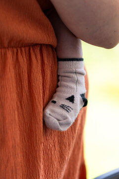 Mother holding newborn baby wearing cute cat pattern sock close up