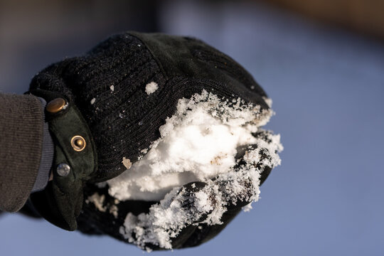 Gloved hand holding a fresh snowball during winter day