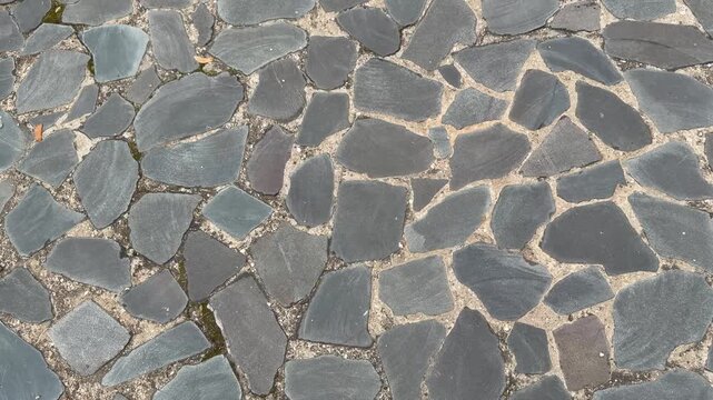 Old cobblestone pavement made of rough grey flat stones and sand under soft daylight outdoors. Ancient flagstone road texture, historical urban flooring material backdrop.