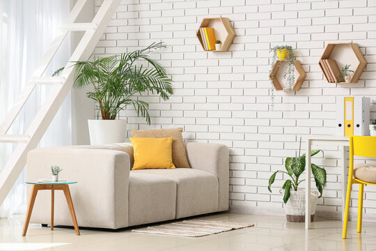 Interior design and home office workspace, modern living room with comfortable sofa and yellow accents in a bright apartment with white brick wall