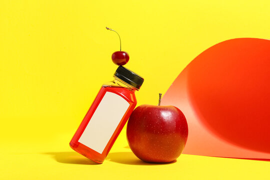 Healthy nutrition and organic lifestyle, red fruit juice bottle with blank label and fresh apple on yellow background with cherry balance