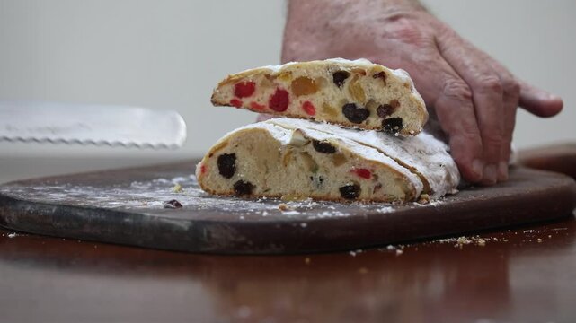 Christstollen, traditional German Christmas fruit bread dusted with powdered sugar and cut into slices, showing the dense crumb studded with candied cherries, candied fruit, raisins and nuts.