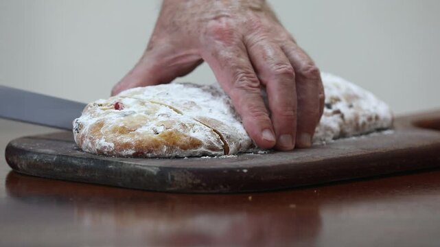 Christstollen, traditional German Christmas fruit bread dusted with powdered sugar and cut into slices, showing the dense crumb studded with candied cherries, candied fruit, raisins and nuts.