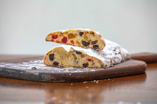 Christstollen, traditional German Christmas fruit bread dusted with powdered sugar and cut into slices, showing the dense crumb studded with candied cherries, candied fruit, raisins and nuts.