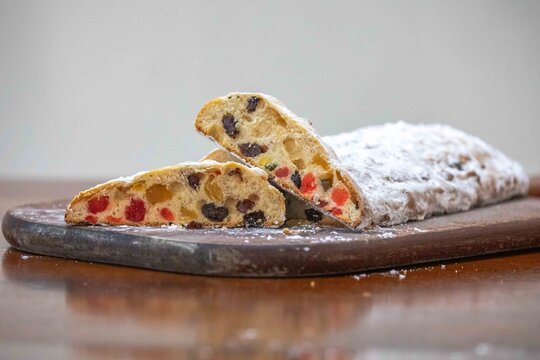 Christstollen, traditional German Christmas fruit bread dusted with powdered sugar and cut into slices, showing the dense crumb studded with candied cherries, candied fruit, raisins and nuts.