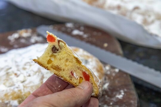 Christstollen, traditional German Christmas fruit bread dusted with powdered sugar and cut into slices, showing the dense crumb studded with candied cherries, candied fruit, raisins and nuts.