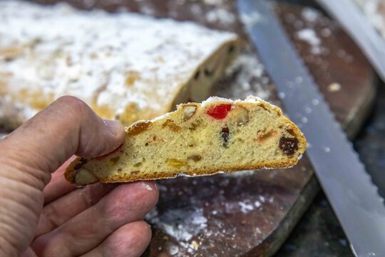 Christstollen, traditional German Christmas fruit bread dusted with powdered sugar and cut into slices, showing the dense crumb studded with candied cherries, candied fruit, raisins and nuts.