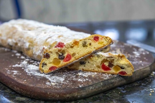 Christstollen, traditional German Christmas fruit bread dusted with powdered sugar and cut into slices, showing the dense crumb studded with candied cherries, candied fruit, raisins and nuts.
