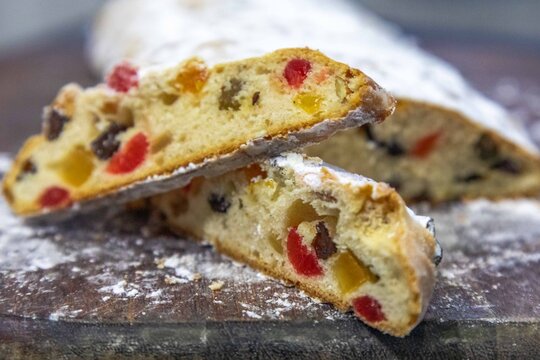 Christstollen, traditional German Christmas fruit bread dusted with powdered sugar and cut into slices, showing the dense crumb studded with candied cherries, candied fruit, raisins and nuts.