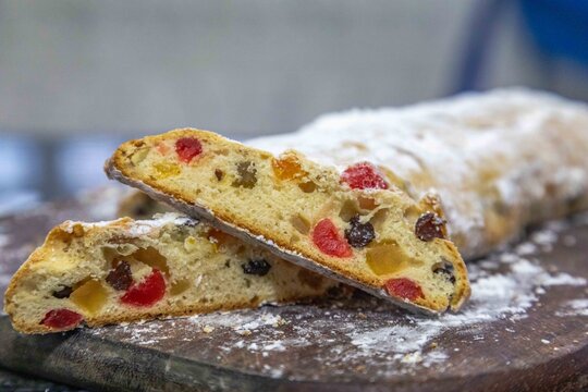 Christstollen, traditional German Christmas fruit bread dusted with powdered sugar and cut into slices, showing the dense crumb studded with candied cherries, candied fruit, raisins and nuts.