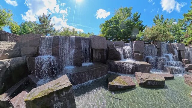 Sunlight falls on angular granite and flowing water beneath dense Roosevelt Memorial greenery.
