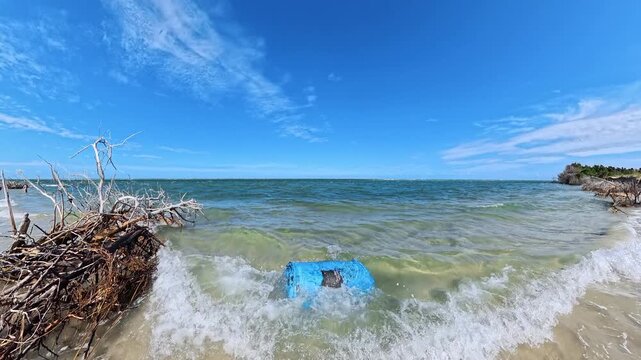Marine debris interrupts clear coastal water beneath a blue sky with clouds.
