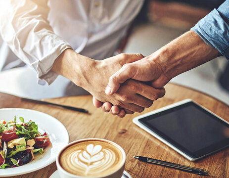 Two professionals seal a successful business deal with a confident handshake over lunch. This warm, professional interaction evokes trust, partnership, and agreement. Ideal for corporate branding.