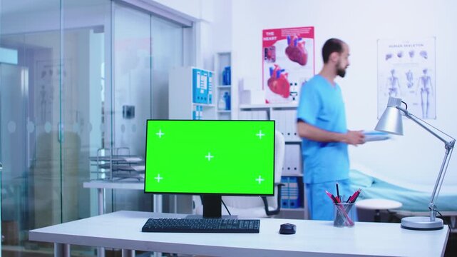 chroma key computer monitor is framed prominently in the clinic while medical staff move through the background, creating healthcare technology copy space.