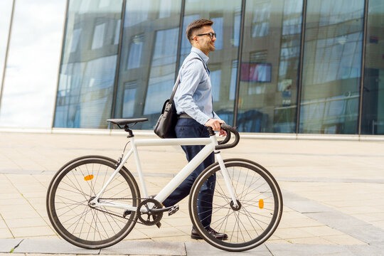 Man walking a bicycle in a modern urban setting under a cloudy sky