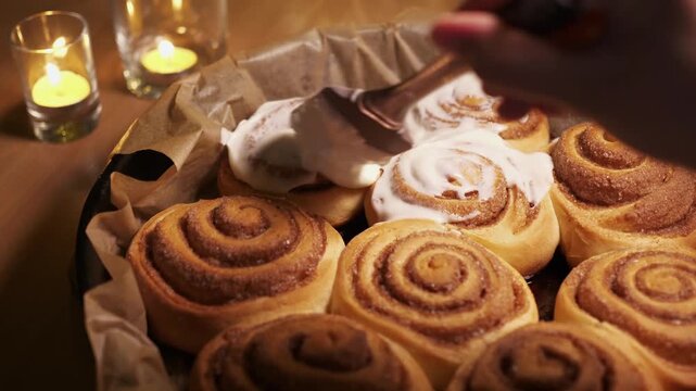 High angle shot of spreading white icing on fresh baked cinnamon rolls with candles