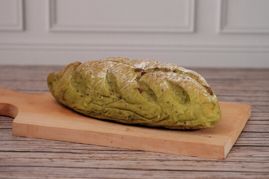 Freshly green sourdough bread rests on a wooden board. Crusty exterior shows artisanal craftsmanship. Soft green hue hints at matcha or herbal infusion. Warm, inviting aroma suggests homemade comfort